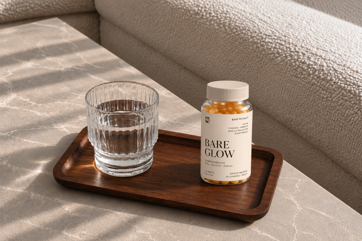 Bare Glow gummies beauté Bare Rituals sur un plateau en bois avec un verre d’eau, dans un intérieur lumineux aux tons naturels.